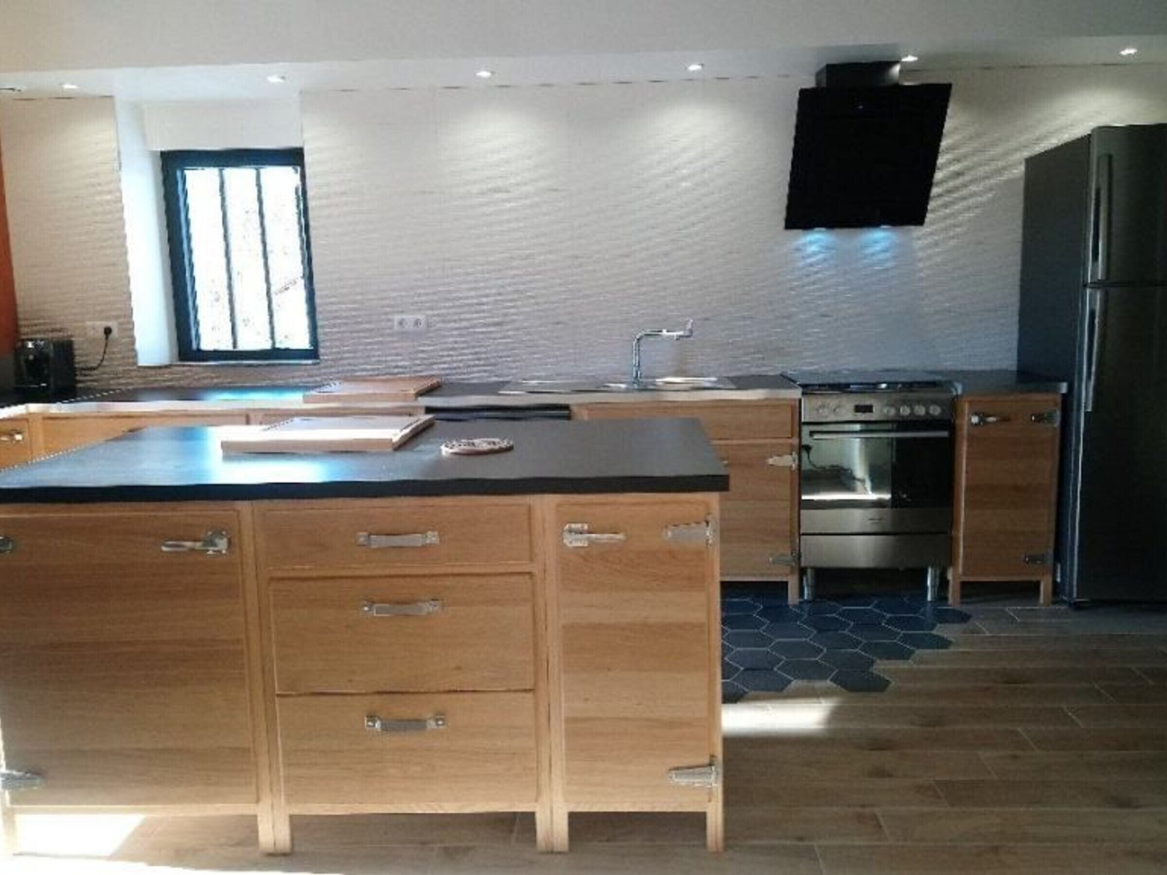 Une cuisine moderne avec des meubles en bois, un plan de travail noir, un four encastré et un réfrigérateur en acier inoxydable.