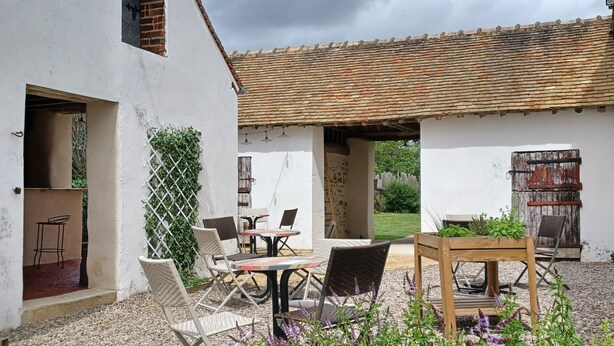 A rustic outdoor seating area with wicker chairs and a table, surrounded by gravel and flowering plants.