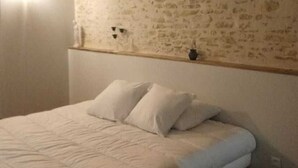 A bedroom with a bed, white bedding, a textured wall, and a small shelf with a vase.