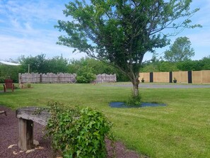 A grassy outdoor area with a wooden fence, a tree, and a bench.