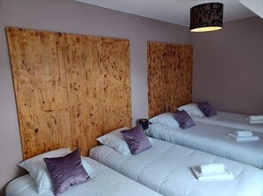 A hotel room with three single beds, each with a wooden headboard, white bedding, and purple pillows.