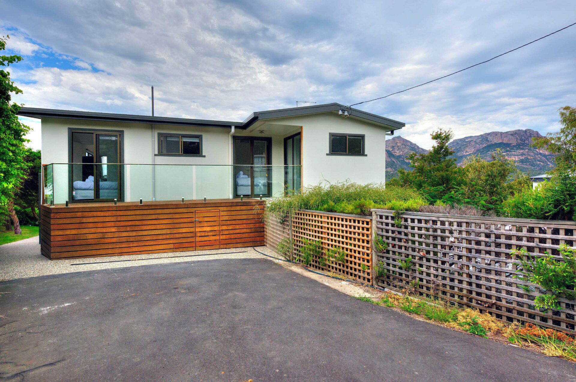 A modern two-story house with a balcony, a wooden fence, and a mountain backdrop.