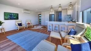 A modern living room with a large window, a kitchen area, and a seating area with a sofa and chairs.