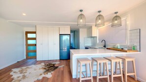 A modern kitchen with a central island, bar stools, pendant lighting, and a refrigerator.
