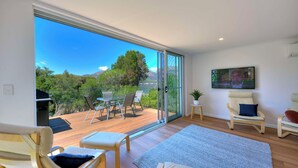 A spacious living area with a large sliding glass door leading to an outdoor deck, a comfortable seating area with a sofa and chairs, and a flat-screen TV mounted on the wall.