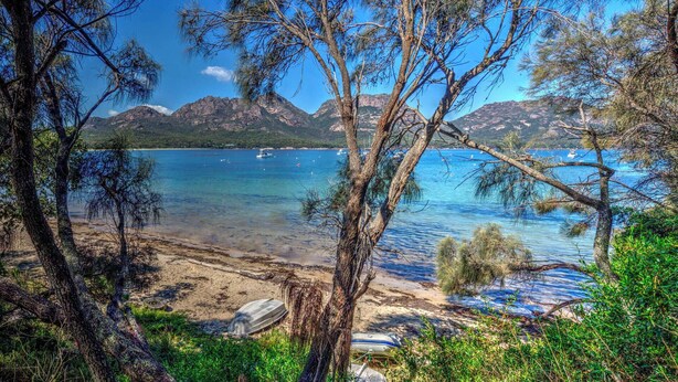 A beach with clear water, boats, and mountains in the background.