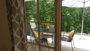 Una habitación con puerta de cristal que da a un patio al aire libre. En el interior, hay una mesa con sillas y un florero con flores.