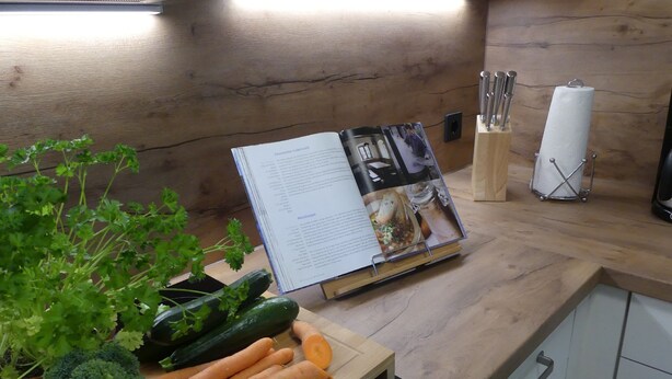 Una encimera de cocina con un libro de recetas, verduras frescas y un bloque de cuchillos.