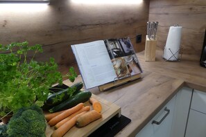 Uma bancada de cozinha com um livro de receitas, legumes frescos e um bloco de facas.