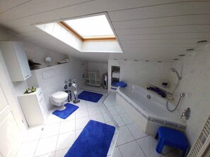 A modern bathroom with a skylight, a bathtub, a shower, and a toilet. - Ferienwohnung Olm (Dolgesheim)