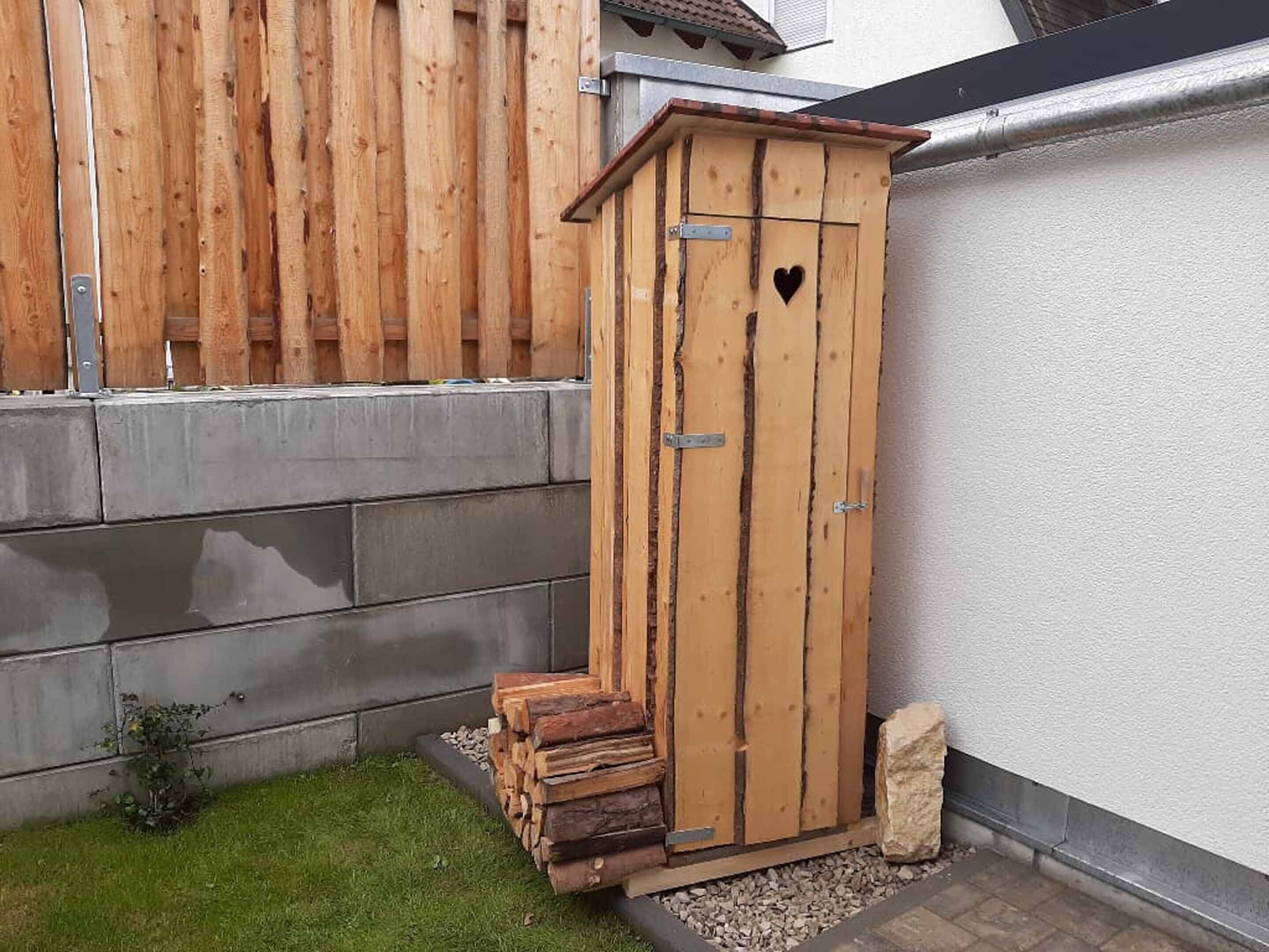 A wooden shed with a heart-shaped cutout, a metal latch, and a small step leading up to it.
