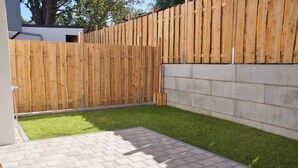A backyard with a wooden fence, a paved patio, and a grassy area.