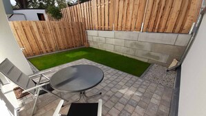 A patio area with a round table and two chairs, a small lawn, and a wooden fence.