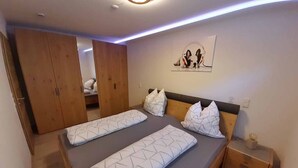 A bedroom with two beds, wooden wardrobe, and a wall-mounted artwork.