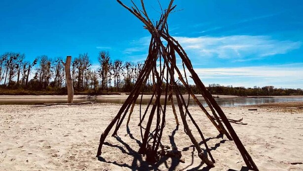 A sand dune with a stick structure in the center, a clear sky, and a body of water in the background. - Ferienwohnung Bellissima (Ering)