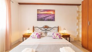 Ein Schlafzimmer mit einem Bett, zwei Nachttischen mit Lampen, einem Holzschrank und einem Gemälde eines Lavendelfeldes an der Wand.