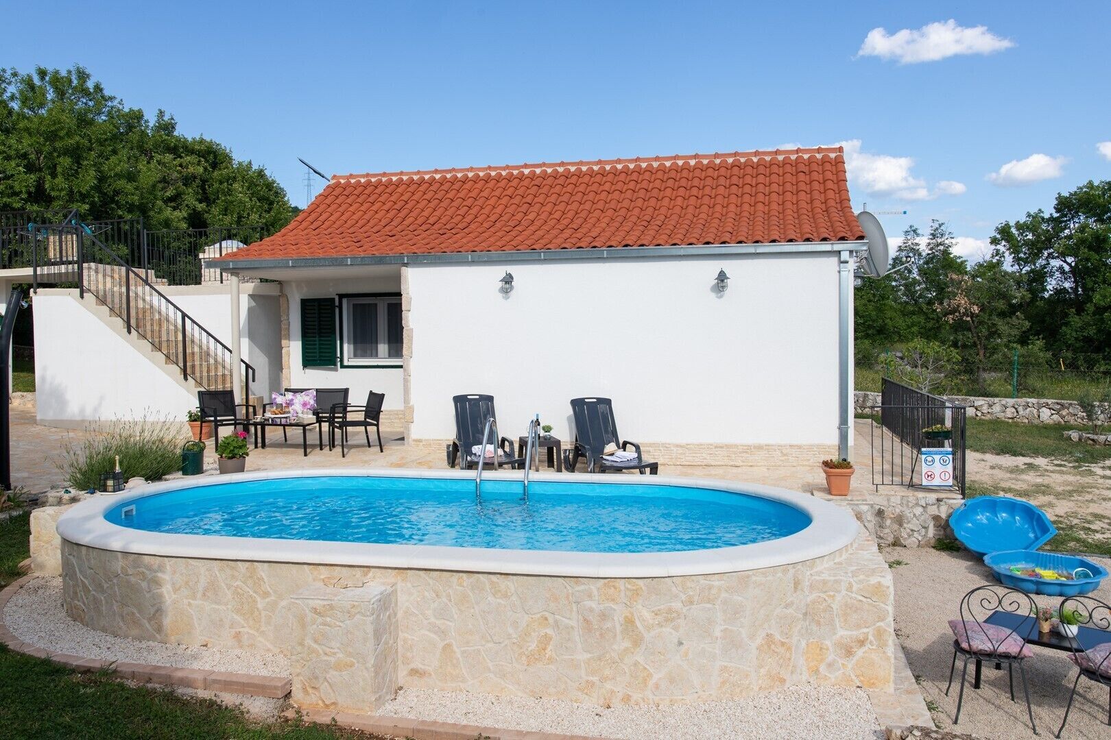 Une maison avec une piscine, une terrasse avec des chaises et un escalier menant à un étage supérieur.