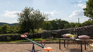 Ein Sandspielplatz mit einem blauen Sandkasten, einer Wippe und einem Tisch mit Stühlen.