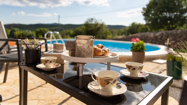 Ein Tisch gedeckt mit Teetassen, Untertassen, einem Teekessel und Gebäck am Pool mit schöner Aussicht.