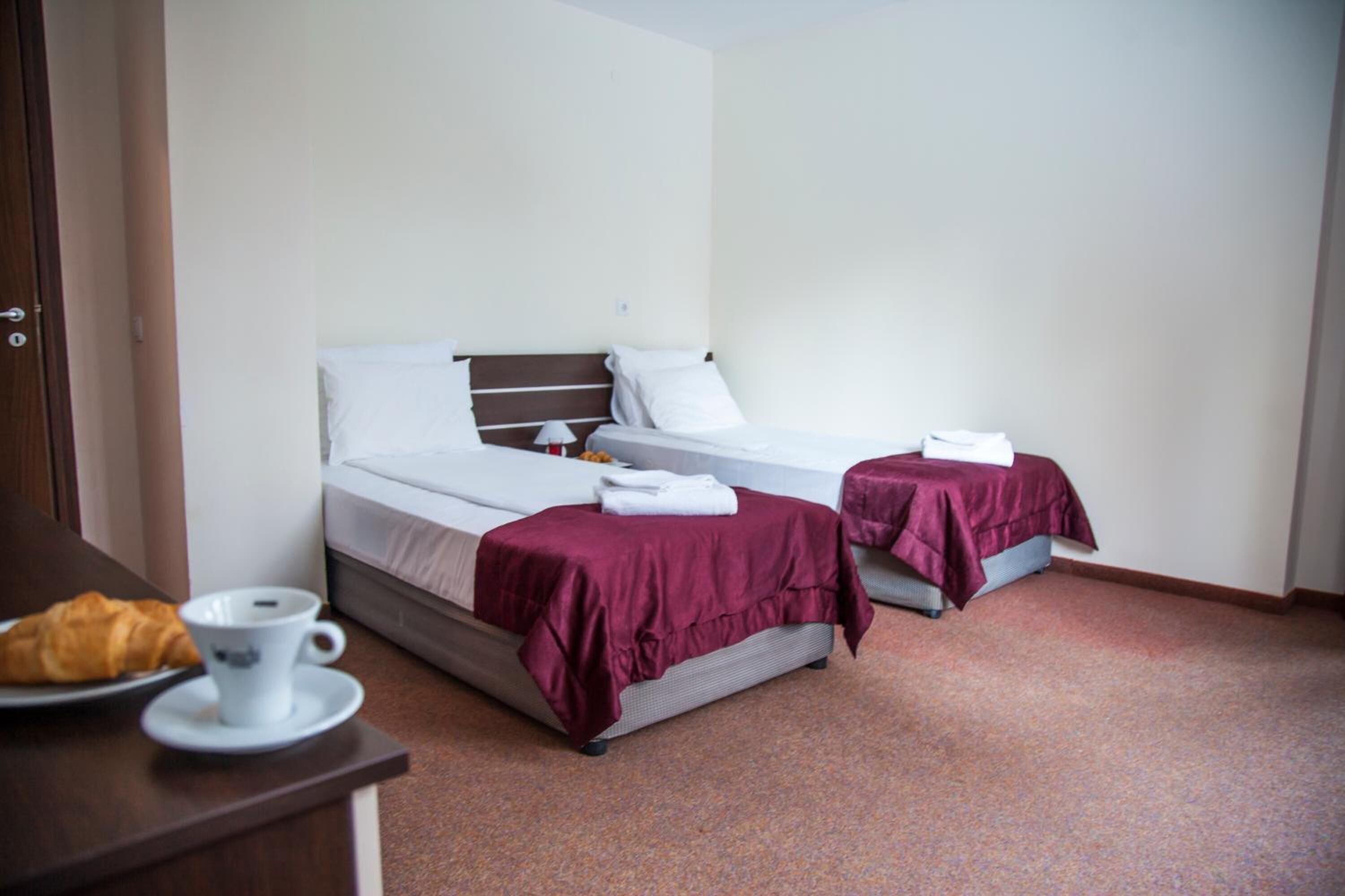 Ein Hotelzimmer mit zwei Einzelbetten, einem kleinen Tisch mit Tasse und Croissant sowie einer Tür.