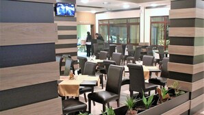 A restaurant with wooden panel walls, black leather chairs, and small potted plants. Tables are set with white tablecloths and napkins. - Borovets Green Hotel (Samokov)
