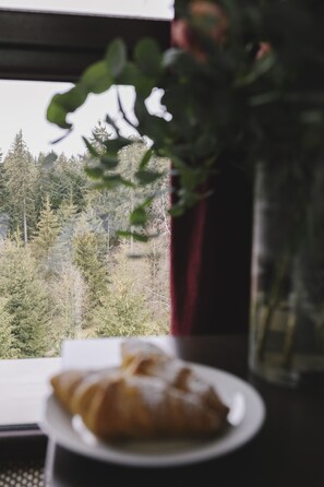 A window with a view of a forest, a plate with a pastry, and a vase with flowers. - Borovets Green Hotel (Samokov)