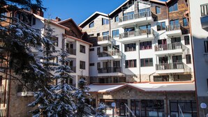 A multi-story hotel with balconies, stone facade, and snow-covered trees. - Borovets Green Hotel (Samokov)
