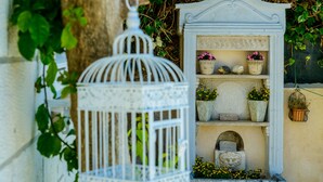 A white birdcage with a decorative design, a stone shelf with potted plants, and a small stone structure with a carved face. - Villa Ida (Dubrovnik)