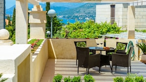 A terrace with a table and chairs, a view of a mountainous landscape, and a body of water. - Villa Ida (Dubrovnik)