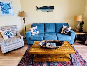 A living room with a blue sofa, patterned armchair, wooden coffee table, and a wall-mounted fish decoration.