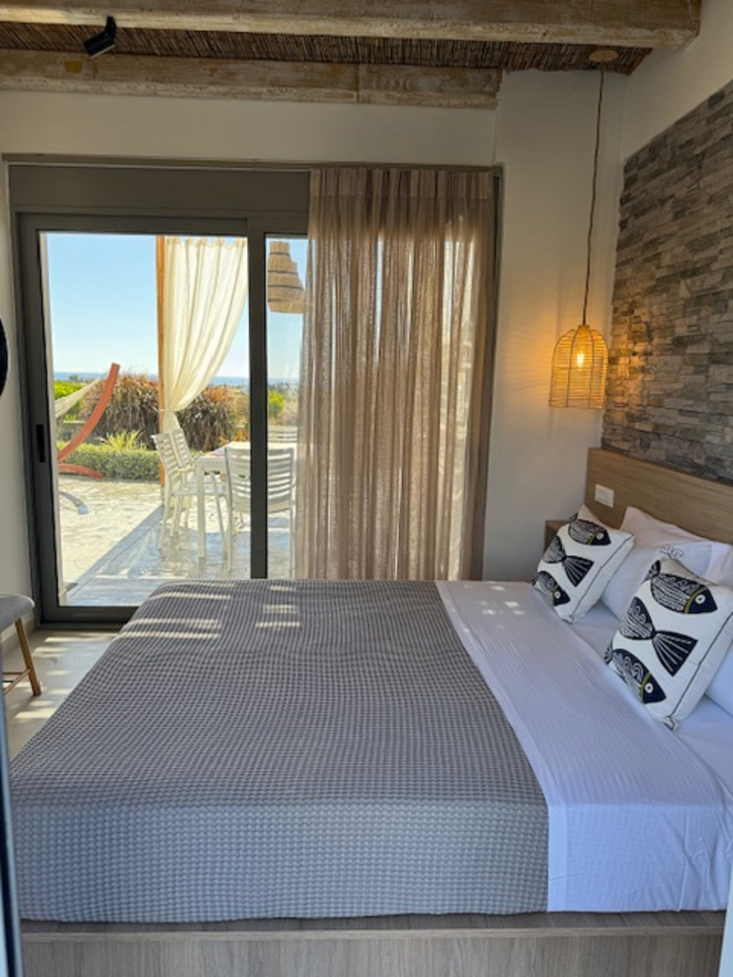 Une chambre à coucher avec un lit, des rideaux, une vue sur l’extérieur, un luminaire suspendu et une tête de lit en bois.
