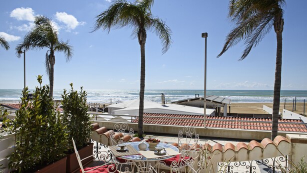 Eine Terrasse mit Esstisch mit Blick auf Strand und Meer.