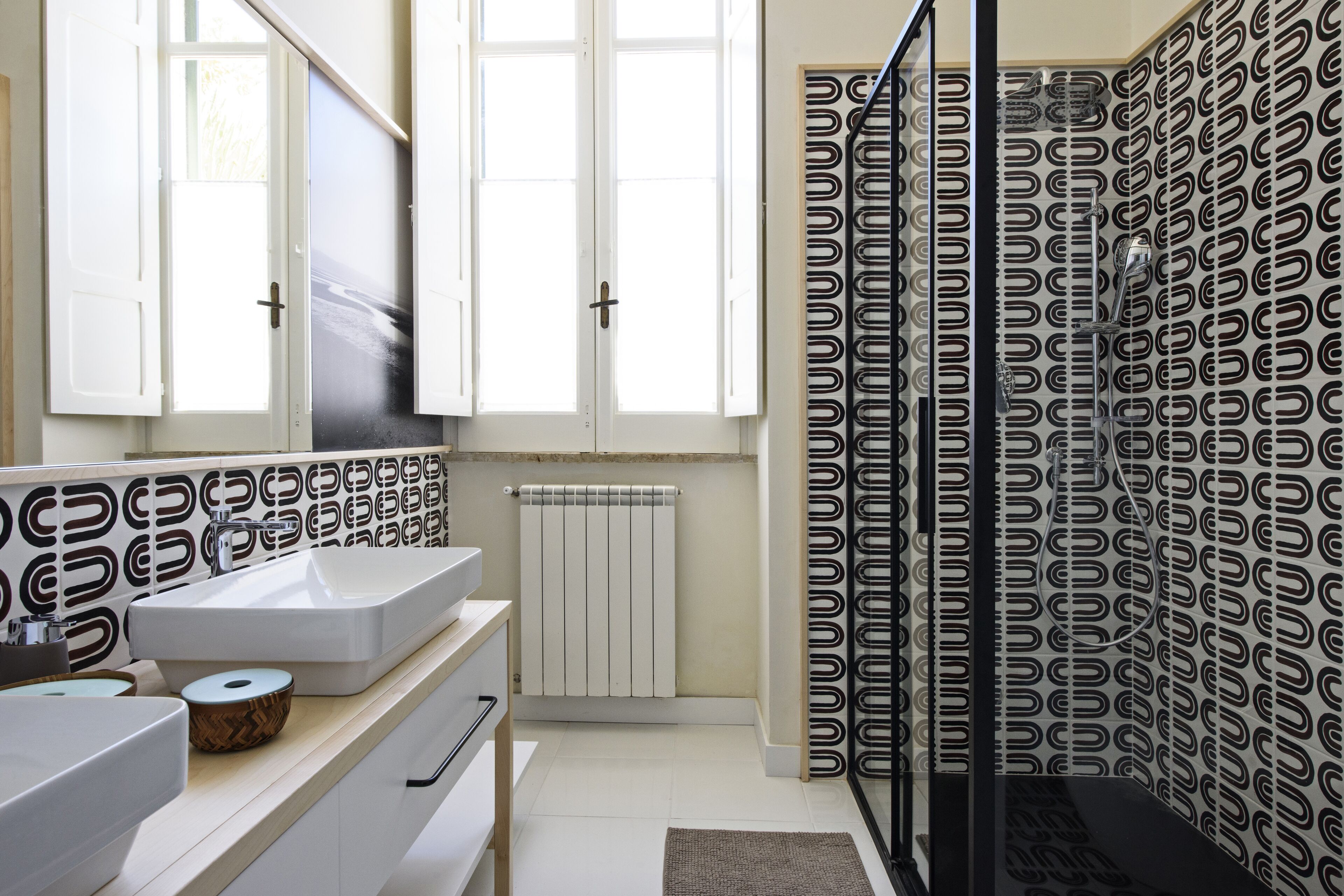 A modern bathroom with a large mirror, white cabinets, a white sink, and a patterned shower curtain.