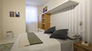 Ein Schlafzimmer mit Bett, Kissen, Nachttisch, Lampe, Kleiderschrank und einem Fenster mit Vorhängen.