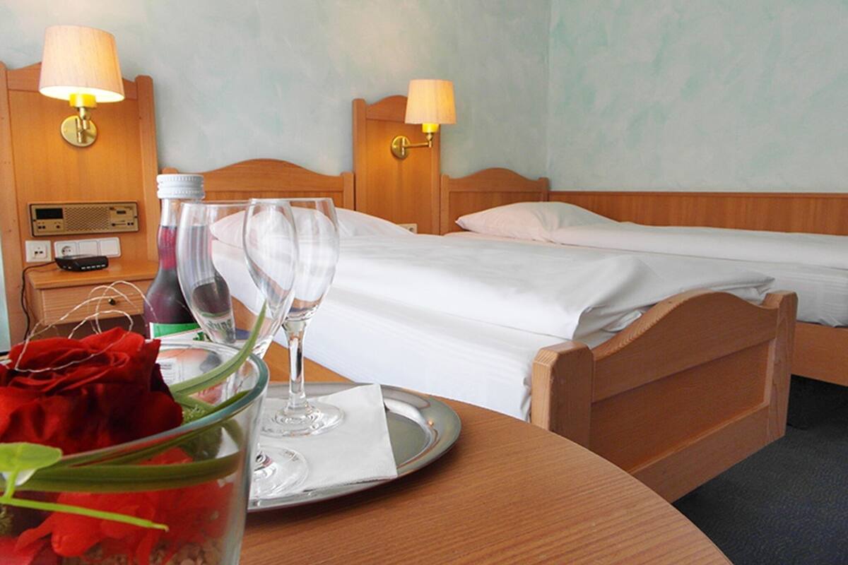 A hotel room with two beds, a bedside table with a radio, a bottle, and two wine glasses on a tray.