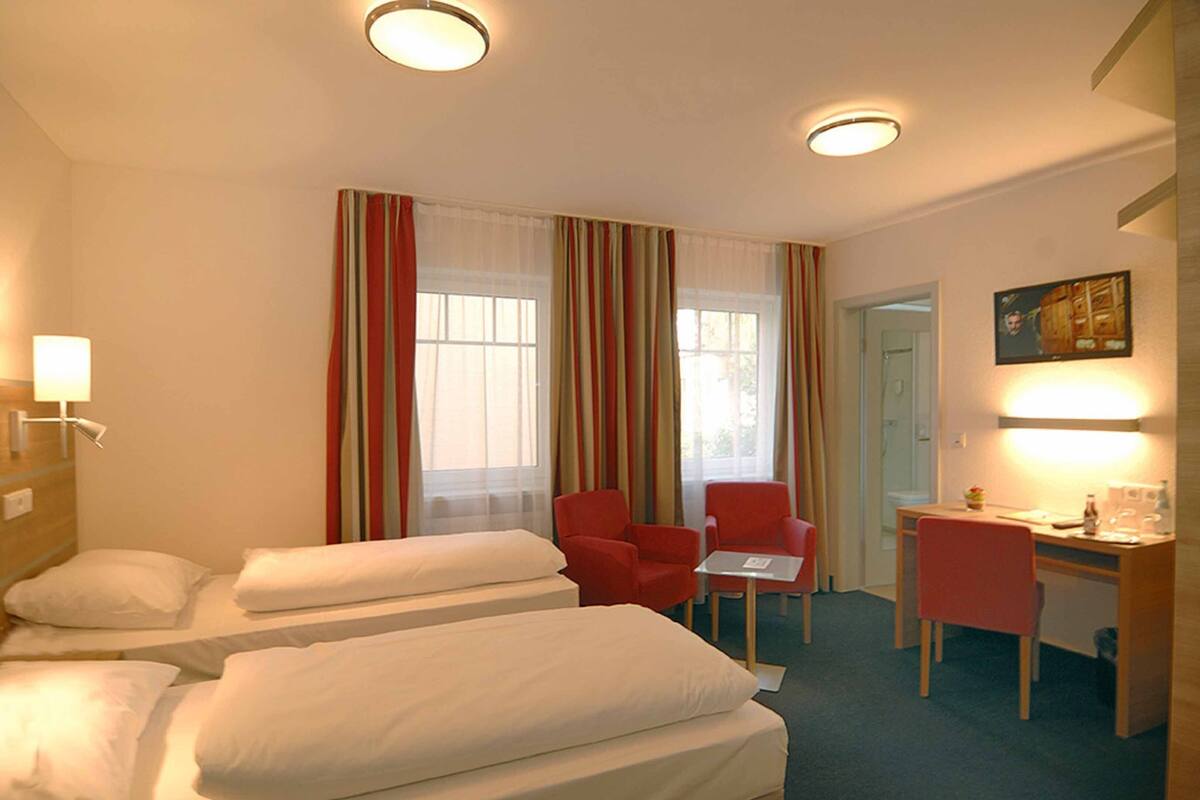 A hotel room with two beds, a desk, a chair, and a small table.
