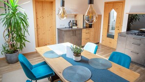 A modern kitchen with wooden cabinets, a dining table with blue chairs, and hanging pendant lights. - Apartment “Lara Ruveda” with Mountain View, Private Terrace and Wi-Fi (St.Ulrich)