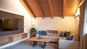 A modern living room with a flat-screen TV, wooden beams, a sofa, and a coffee table. - Apartment “Lara Ruveda” with Mountain View, Private Terrace and Wi-Fi (St.Ulrich)