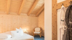A wooden room with a bed, a chair, a robe, and a nightstand. - Apartment “Lara Ruveda” with Mountain View, Private Terrace and Wi-Fi (St.Ulrich)