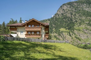 Un chalet doté d’un balcon en bois, d’une cour clôturée et surplombant un paysage montagneux.