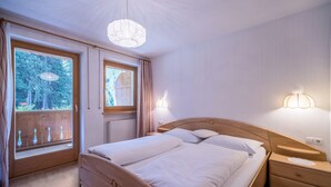 Makuuhuoneessa on puinen sänky, yöpöydät, ikkuna, jossa on verhot, ja kattokruunu.