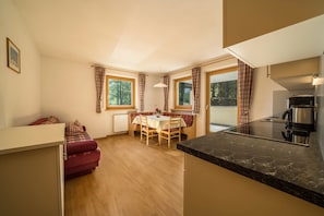 A compact room with a dining table, a sofa, a kitchen area with a stove, and large windows.