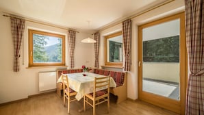 Ein Zimmer mit Holztisch, Sitzbank, Heizkörper und großen Fenstern mit Vorhängen.