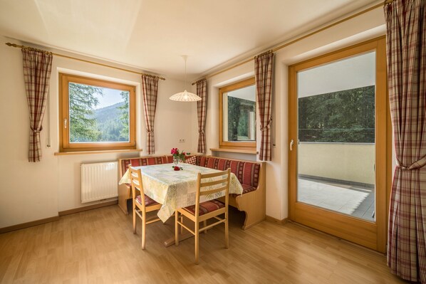 Una habitación con una mesa de madera, bancos, un radiador y ventanas amplias con cortinas.