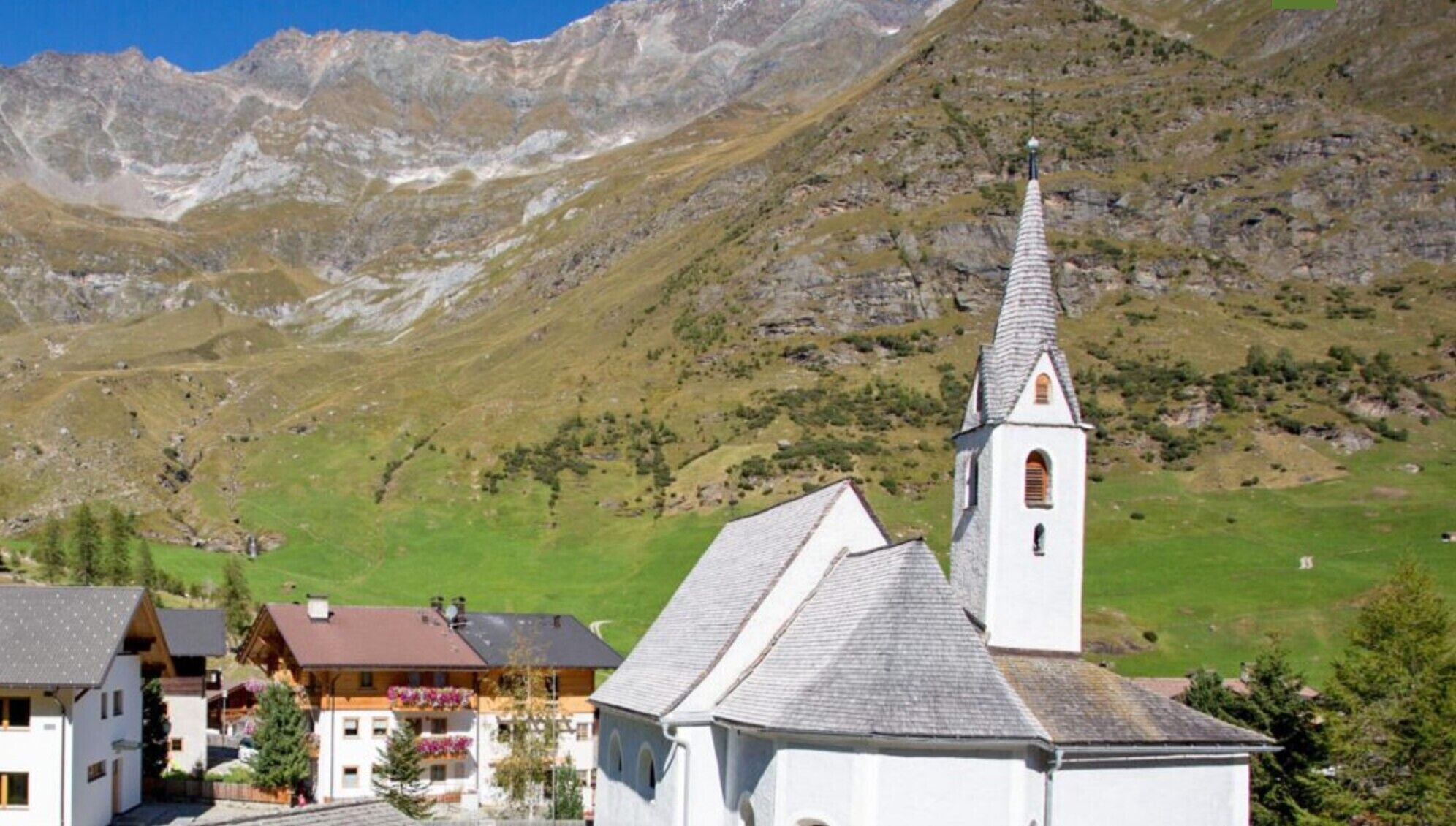 A mountain village with a church, houses, and a clear view of the surrounding mountains.