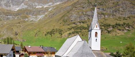 A mountain village with a church, houses, and a clear view of the surrounding mountains.