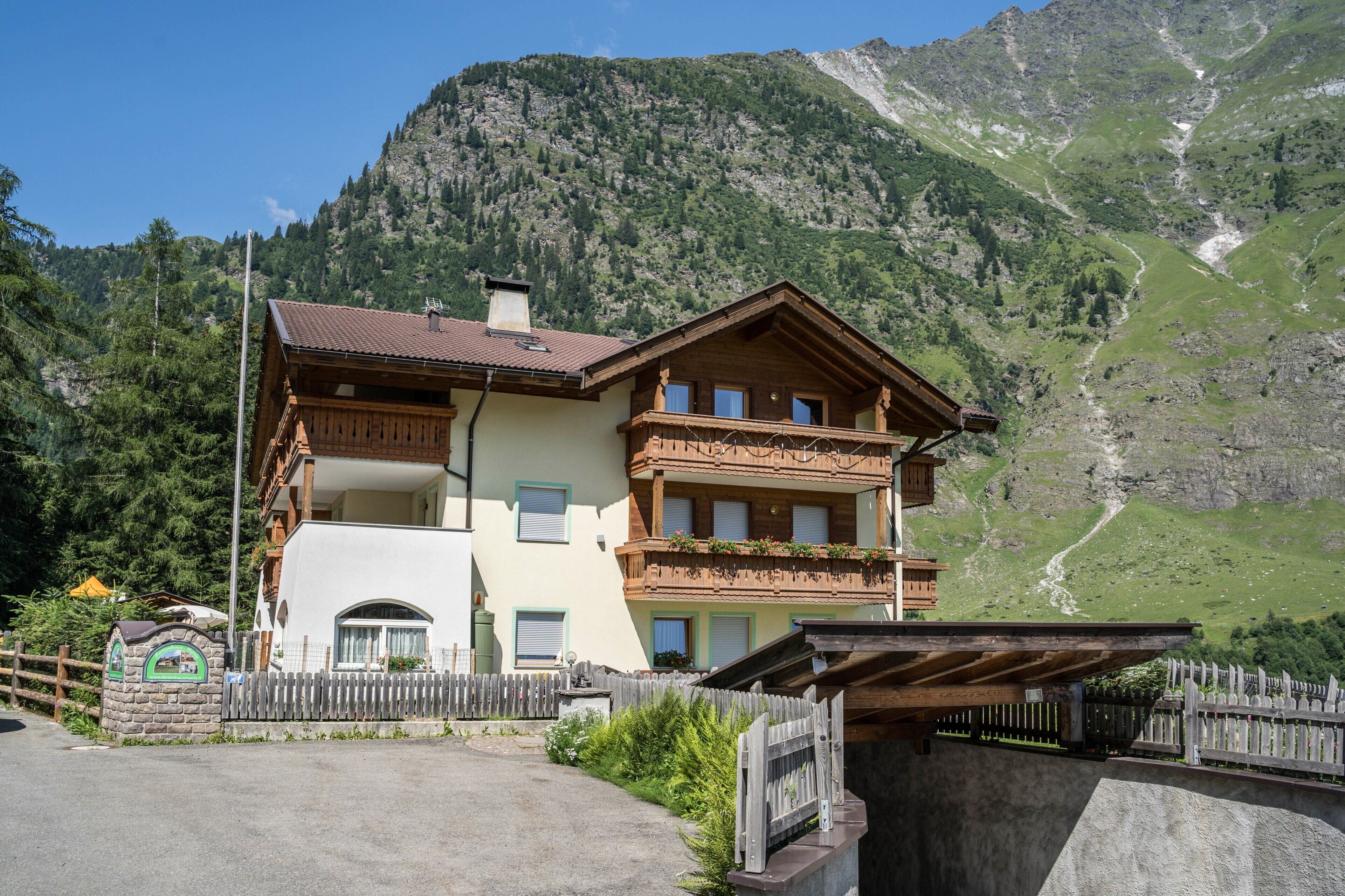 A two-story wooden house with balconies, a stone mailbox, and a mountain backdrop.