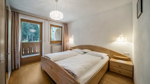 Ein Schlafzimmer mit einem hölzernen Bett, Nachttischlampen, einem Fenster mit Vorhängen und Blick ins Grüne.