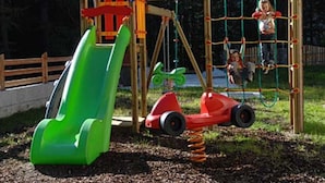 Ein Spielplatz mit Rutsche, Schaukeln und einer kleinen Rundfahrt mit Autos.