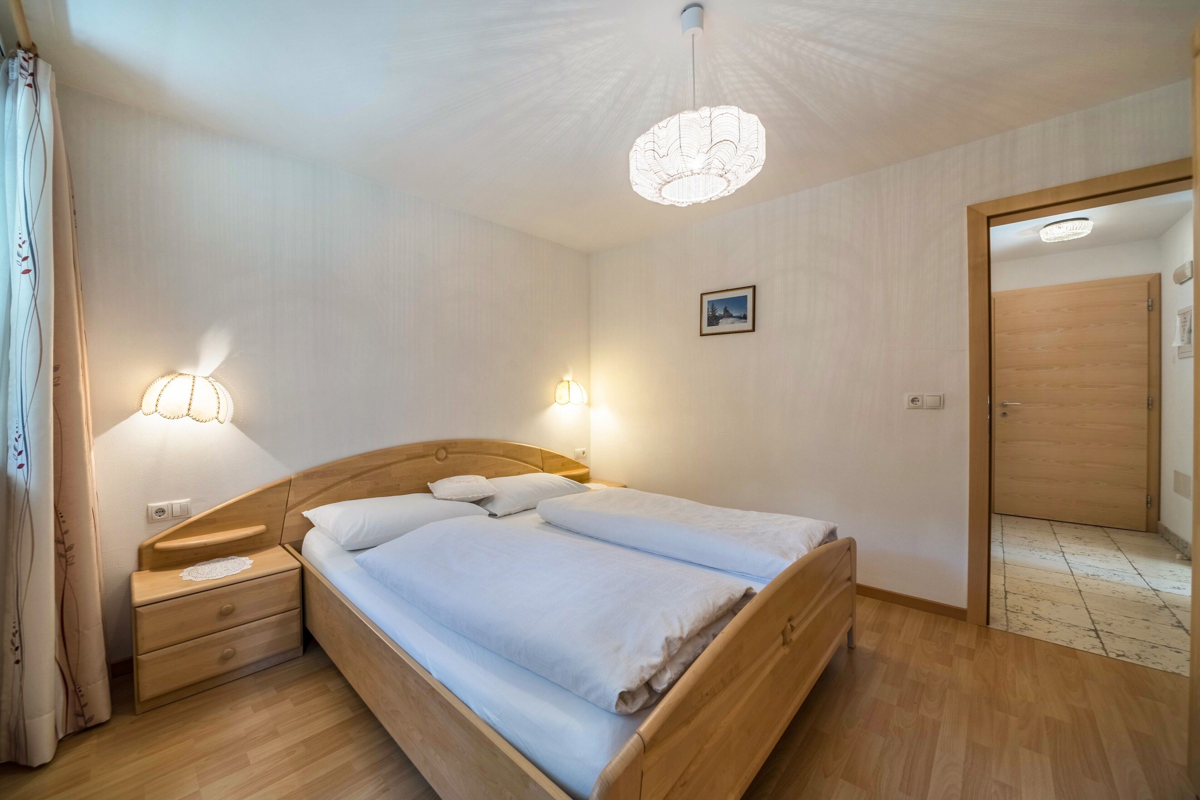 Un letto rifatto con cura, una testiera in legno, abat-jour e un comodino con lampada.
